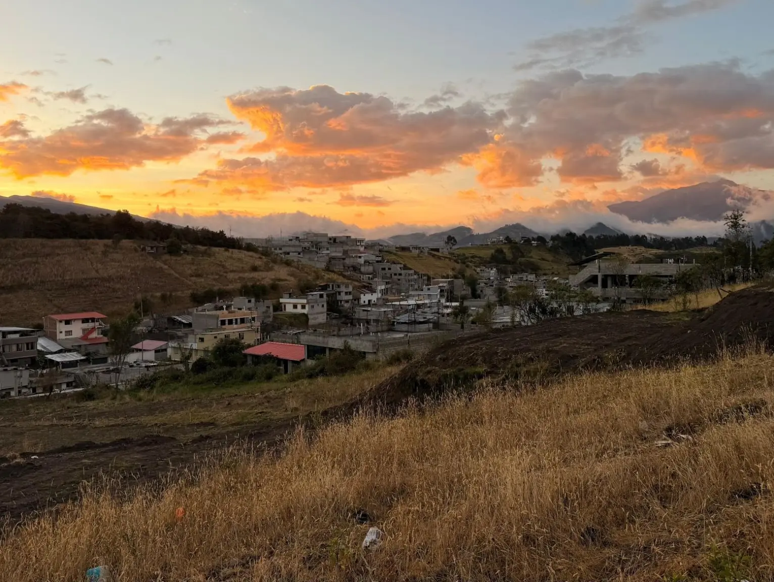 Atardecer naranja sobre el barrio y las montañas, visto desde el terreno del proyecto La Cocha en el sur de Quito